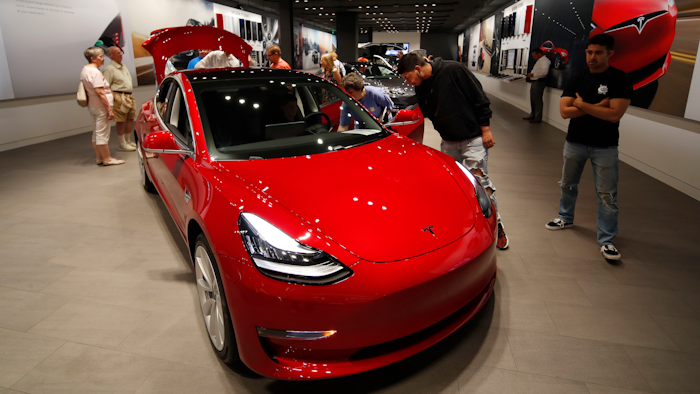 In this Friday, July 6, 2018, photograph, prospective customers confer with sales associates as a Model 3 sits on display in a Tesla showroom in the Cherry Creek Mall in Denver.
