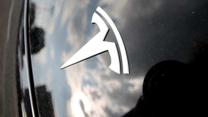 In this July 8, 2018, photo, clouds are reflected above the company logo on the hood of a 2018 Model 3 sedan on display outside a Tesla showroom in Littleton, Colo.