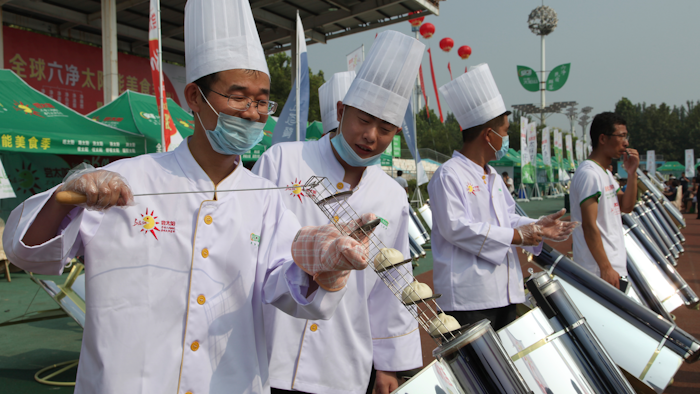 In this photo taken Thursday, Aug. 2, 2018, chefs prepare to cook buns in a solar cooker that using a metal and glass vacuum tube heated by mirrors curved to capture the sun's heat.