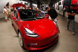 In this Friday, July 6, 2018, photograph, prospective customers confer with sales associates as a Model 3 sits on display in a Tesla showroom in the Cherry Creek Mall in Denver.