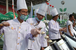 In this photo taken Thursday, Aug. 2, 2018, chefs prepare to cook buns in a solar cooker that using a metal and glass vacuum tube heated by mirrors curved to capture the sun's heat.