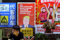 In this Monday, Aug. 13, 2018, photo, a man stands near a poster depicting a mural of U.S. President Donald Trump outside a restaurant in Guangzhou.