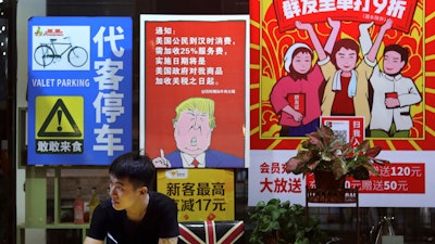 In this Monday, Aug. 13, 2018, photo, a man stands near a poster depicting a mural of U.S. President Donald Trump outside a restaurant in Guangzhou.