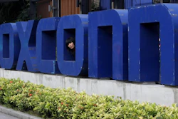 In this May 27, 2010 file photo, a worker looks out through the logo at the entrance of the Foxconn complex in the southern Chinese city of Shenzhen.