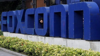 In this May 27, 2010 file photo, a worker looks out through the logo at the entrance of the Foxconn complex in the southern Chinese city of Shenzhen.