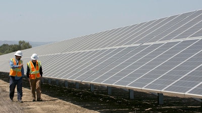 In this Aug. 17, 2017, file photo, solar tech Joshua Valdez, left, and senior plant managerTim Wisdom walk past solar panels at a Pacific Gas and Electric Solar Plant, in Dixon, Calif.