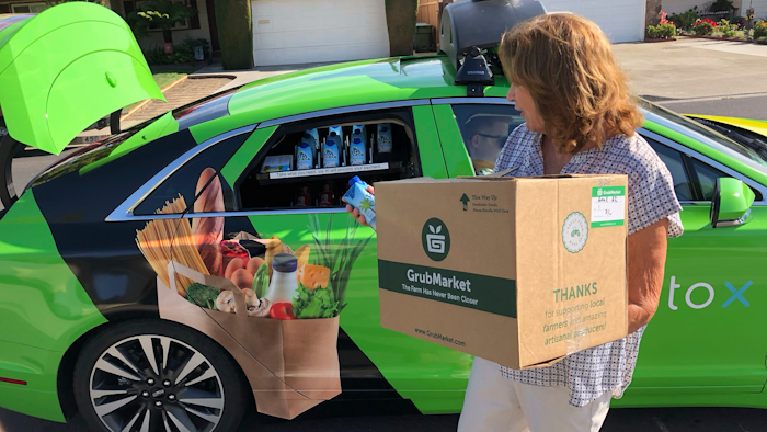 In this Aug. 29, 2018 photo, customer Maureen Blaskovich grabs a coconut water from the backseat window of a self-driving car in San Jose, Calif.