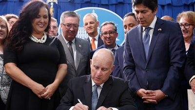 State Sen. Kevin de Leon, D-Los Angeles, right, watches as Gov. Jerry Brown, center, signs his environmental measure SB100 into law, Monday, Sept. 10, 2018, in Sacramento, Calif.