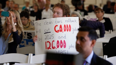 Benjamin Tuggy holds a sign while listening to speakers during the first of three public hearings on the Trump administration's proposal to roll back car-mileage standards in a region with some of the nation's worst air pollution Monday, Sept. 24, 2018 in Fresno, Calif.