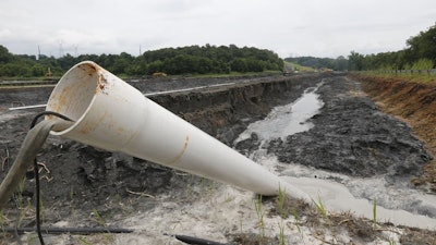 In this Friday June 26, 2015 file photo, a drain pipe sticks out of a coal ash retention pond at the Dominion Power’s Possum Point Power Station in Dumfries, Va.