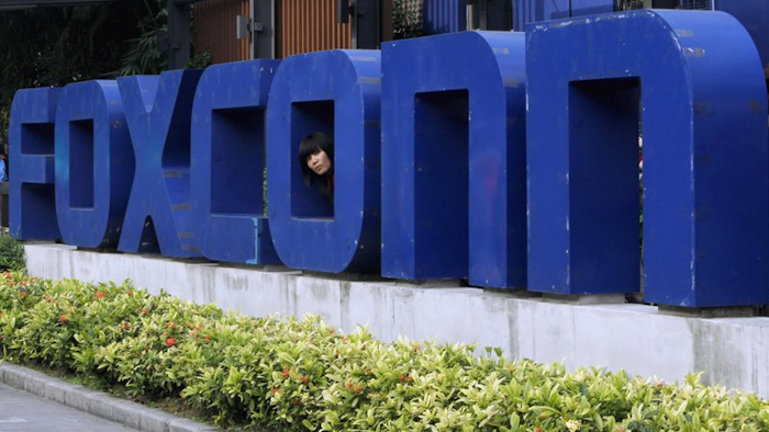 In this May 27, 2010 file photo, a worker looks out through the logo at the entrance of the Foxconn complex in the southern Chinese city of Shenzhen.