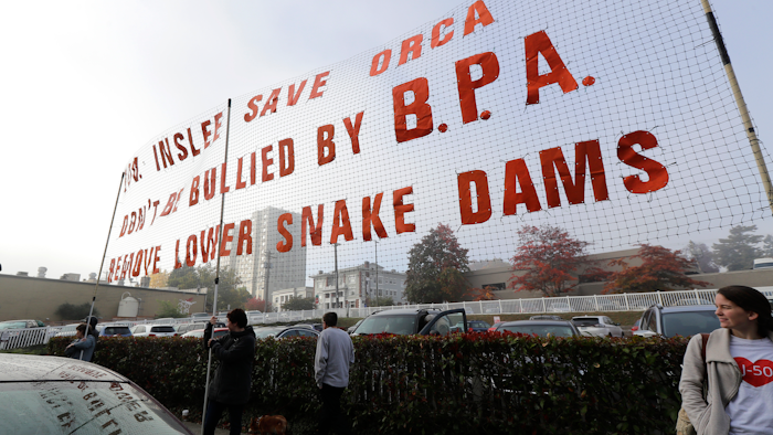 In this Oct. 17, 2018 photo, supporters of dam removals and other measures intended to help endangered orca whales stand near a large sign a outside a building in Tacoma, Wash.