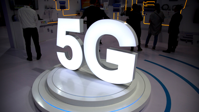 In this Sept. 26, 2018, file photo visitors stand near a 5G logo at a display for Chinese fiber optic cable maker YOFC at the PT Expo in Beijing.