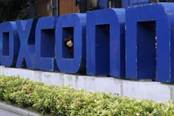 In this May 27, 2010 file photo, a worker looks out through the logo at the entrance of the Foxconn complex in the southern Chinese city of Shenzhen.