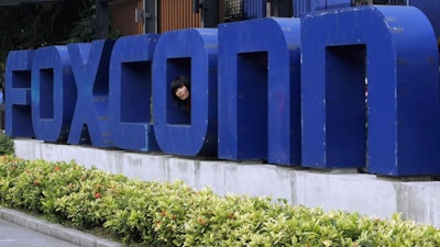 In this May 27, 2010 file photo, a worker looks out through the logo at the entrance of the Foxconn complex in the southern Chinese city of Shenzhen.