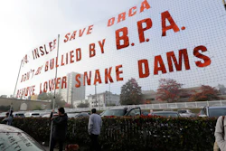 In this Oct. 17, 2018 photo, supporters of dam removals and other measures intended to help endangered orca whales stand near a large sign a outside a building in Tacoma, Wash.