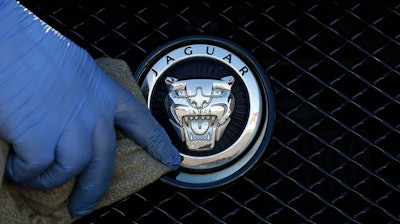 In this file photo taken on Wednesday, Sept. 28, 2016, a worker polishes a Jaguar logo on a car at a Jaguar dealer in London.