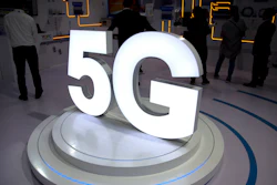 In this Sept. 26, 2018, file photo visitors stand near a 5G logo at a display for Chinese fiber optic cable maker YOFC at the PT Expo in Beijing.