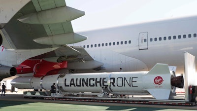 In this Thursday, Oct. 25, 2018, photo released by Virgin Orbit, a completed LauncherOne rocket hangs from the wing of Cosmic Girl, a special Boeing 747 aircraft that is used as the rocket's 'flying launch pad,' at the Long Beach Airport in Long Beach, Calif.