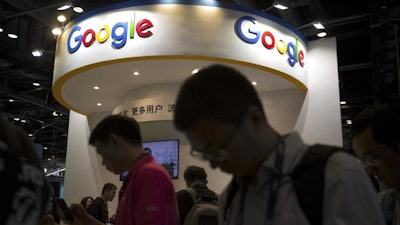 In this April 27, 2017 photo, visitors use their smartphones in front of a booth for Google at the Global Mobile Internet Conference in Beijing.