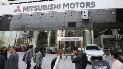 People walk past the headquarters of Mitsubishi Motors Corp. in Tokyo, Monday, Nov. 26, 2018.