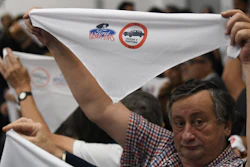 Family members of ex-Ford Motor Co. employees hold up handkerchiefs that are stamped with a message that reads in Spanish: “Ford never more.”