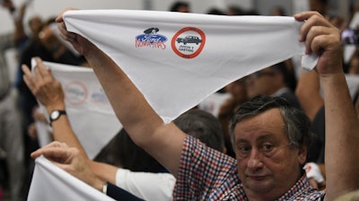 Family members of ex-Ford Motor Co. employees hold up handkerchiefs that are stamped with a message that reads in Spanish: “Ford never more.”