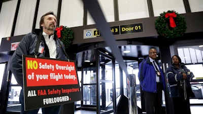 In this Tuesday, Jan. 8, 2019, file photo, FAA employee Michael Jessie holds a sign at Newark Liberty International Airport.