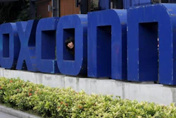 In this May 27, 2010 file photo, a worker looks out through the logo at the entrance of the Foxconn complex in the southern Chinese city of Shenzhen.