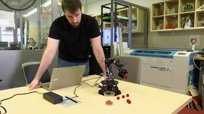 In this image made from a Feb. 1, 2019, video, Robert Kwiatkowski, a graduate student at Columbia University, demonstrates a robotic arm picking up a red ball and dropping it in a cup.