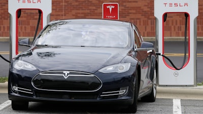 In this June 24, 2017, file photo, a Tesla Model 3 car recharges at at Cochran Commons shopping center in Charlotte, N.C.