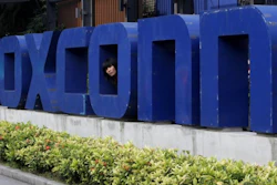 In this May 27, 2010 file photo, a worker looks out through the logo at the entrance of the Foxconn complex in the southern Chinese city of Shenzhen.