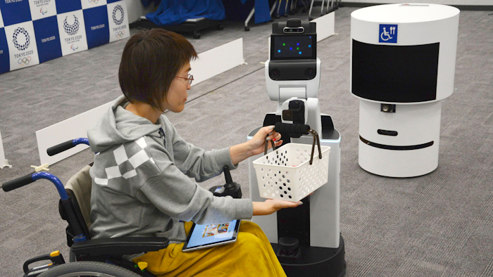 A robot passes a basket containing drinks to a woman in wheelchair during an unveiling event in Tokyo Friday, March 15, 2019. Organizers on Friday showed off robots that will be used at the new National Stadium to provide assistance for fans using wheelchairs.
