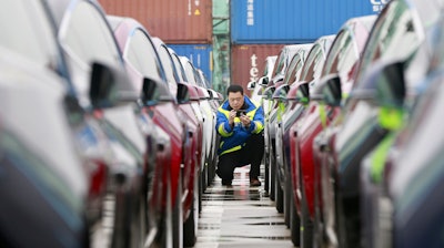 In this Feb. 22, 2019, photo, a port worker works among one of the first batches of Tesla Model 3 electric cars to be delivered to China at a port in Shanghai.