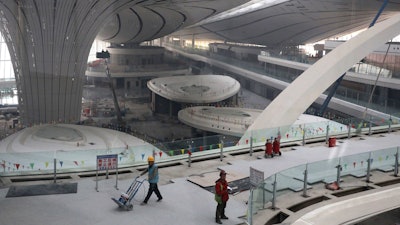 Workers pass through the terminal of the Beijing Daxing International Airport under construction on the outskirts of Beijing, Friday, March 1, 2019.