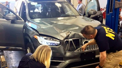 In this March 20, 2018, file photo, investigators examine a driverless Uber SUV that fatally struck a woman in Tempe, Ariz.