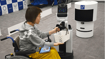 A robot passes a basket containing drinks to a woman in wheelchair during an unveiling event in Tokyo Friday, March 15, 2019. Organizers on Friday showed off robots that will be used at the new National Stadium to provide assistance for fans using wheelchairs.