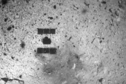 In this Feb. 22, 2019, file photo, this image released by the Japan Aerospace Exploration Agency (JAXA) shows the shadow, center above, of the Hayabusa2 spacecraft after its successful touchdown on the asteroid Ryugu. Japan's space agency says its Hayabusa2 spacecraft will follow up last month's touchdown on a distant asteroid with another risky mission — to drop an explosive to make a crater and collect underground samples to get possible clues to the origin of the solar system.