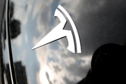 In this July 8, 2018, photo, clouds are reflected above the company logo on the hood of a 2018 Model 3 sedan on display outside a Tesla showroom in Littleton, Colo.