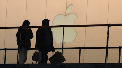 In this Jan. 3, 2019, file photo, shoppers pass by the Apple store logo at a shopping mall in Beijing.