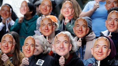 In this Oct. 31, 2018, file photo, demonstrators hold images of Amazon CEO Jeff Bezos near their faces during a protest over the company's 'Rekognition' facial recognition system.