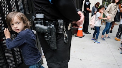 In this Monday May 13, 2019 photo, Julian Richner, 9, leaves school for the day to meet his mother as he passes behind a security guard at Beverly Hills Unified School District's K-8 Horace Mann School in Beverly Hills, Calif.