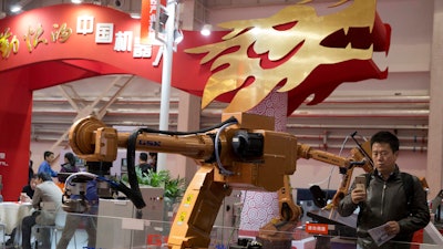 In this Friday, Oct. 21, 2016 photo, visitors look at industrial robots displayed during the World Robot Conference in Beijing.