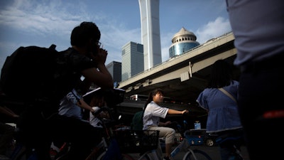 People wait cross the street in a crosswalk in the central business district in Beijing, Friday, May 24, 2019.
