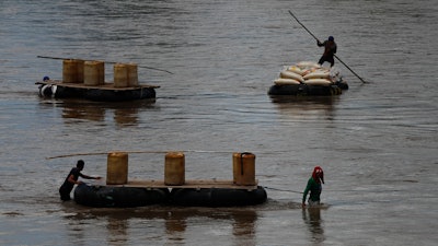 Men use rafts to transport black-market gasoline across the Suchiate River from Guatemala to Mexico, as one pushes sacks of corn in the opposite direction to Guatemala, near Ciudad Hidalgo, Mexico, Thursday, June 6, 2019.