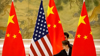 In this Feb. 14, 2019, file photo, Chinese staffers adjust U.S. and Chinese flags before the opening session of trade negotiations between U.S. and Chinese trade representatives at the Diaoyutai State Guesthouse in Beijing. Beijing on Friday, June 28, 2019, criticized what it calls 'negative content' about China in legislation before the U.S. Congress, saying it would further damage relations already roiled by disputes over trade and technology.