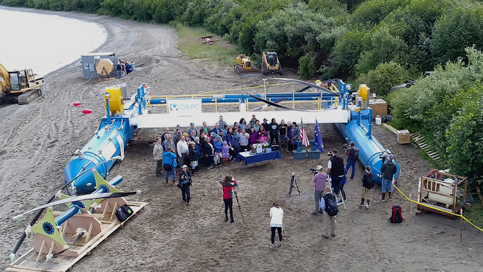 In this Tuesday, July 16, 2019, drone photo released by the University of Alaska Fairbanks and Alaska Center for Energy and Power, Gov. Mike Dunleavy, center rear, poses for photos in front of a Riv-Gen Power System turbine on the bank of the Kvichak River in Igiugig, Alaska. A tiny Alaska Native village is adopting an emerging technology to transform the power of a local river into a renewable energy source.