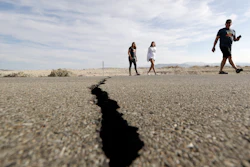 Visitors cross highway 178 next to a crack left on the road by an earthquake Sunday, July 7, 2019, near Ridgecrest, Calif.