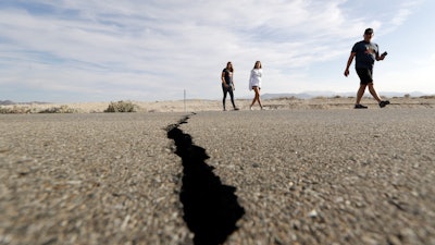 Visitors cross highway 178 next to a crack left on the road by an earthquake Sunday, July 7, 2019, near Ridgecrest, Calif.