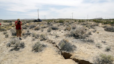 A visitor takes a photo of a crack on the ground following recent earthquakes Sunday, July 7, 2019, outside of Ridgecrest, Calif.